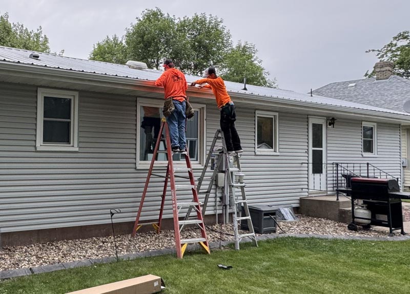 gutter-installation Professional roofing team in high-visibility work gear securely installing seamless gutter systems on a residential property exterior.