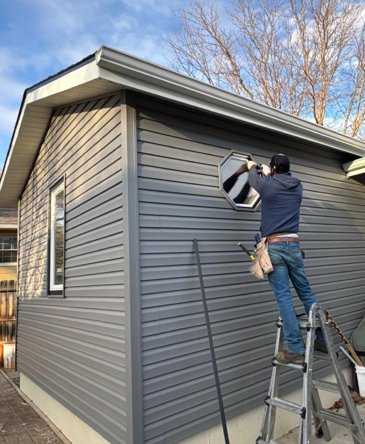 installing-window Professional contractor on a ladder carefully installing a custom octagonal window on a home with dark gray siding