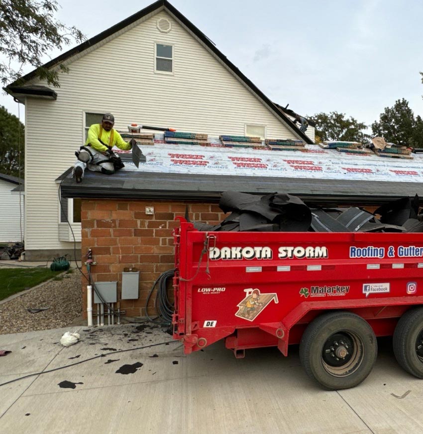 roof-company-dakota Dakota Storm Roofing technician installing premium shingles during a residential roof replacement project, utilizing a branded Equipter debris trailer to maintain a clean and safe job site
