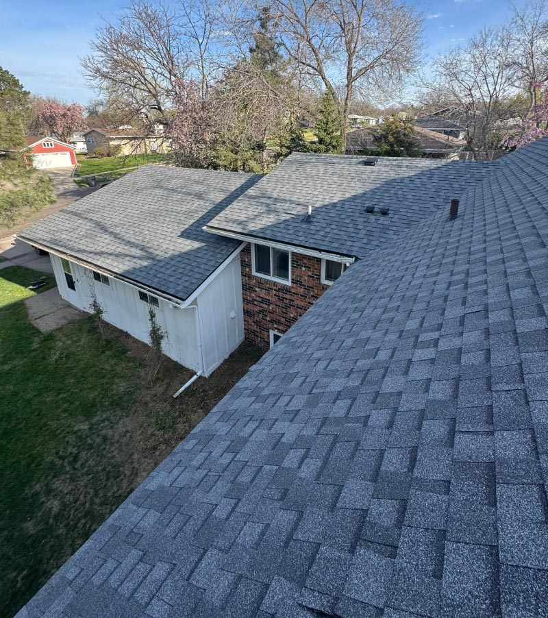 shingle-roof "Aerial view of a residential home with a newly installed dark gray shingle roof, representing durable roofing solutions provided by Dakota Storm Roofing LLC.